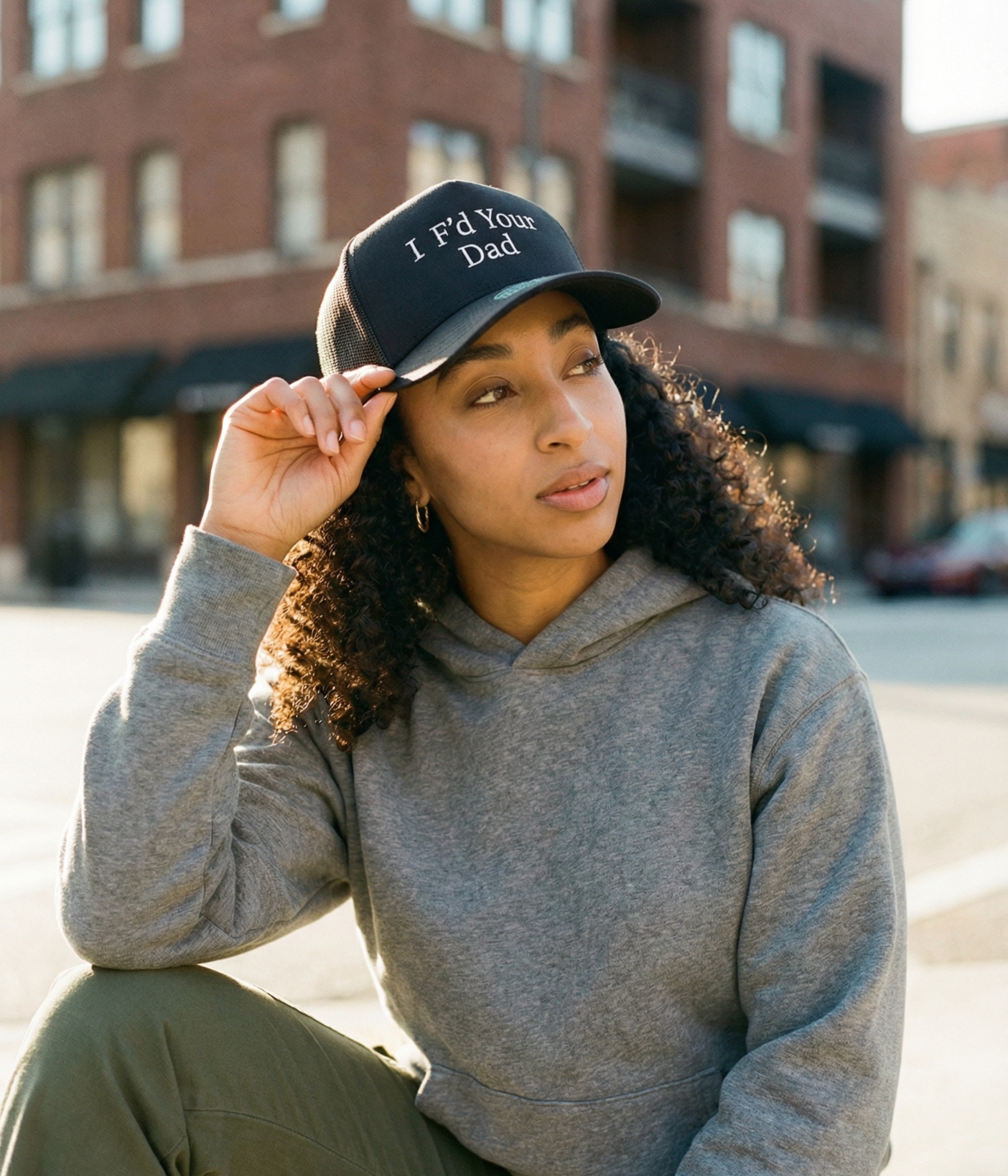 Woman wearing a cap with 'I'd Your Dad' text in an urban setting