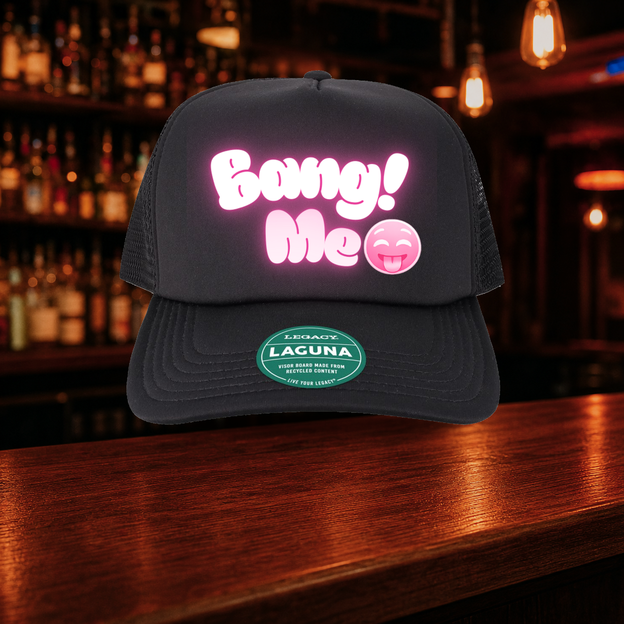Bang Me Trucker Hat — All Black variety shown against a warm after-dark bar backdrop