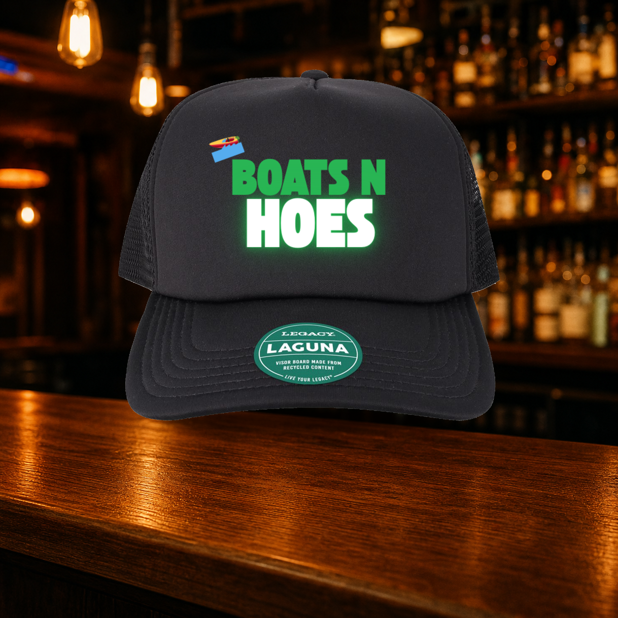 Boats N' Hoes Trucker Hat shown against a warm after-dark bar backdrop