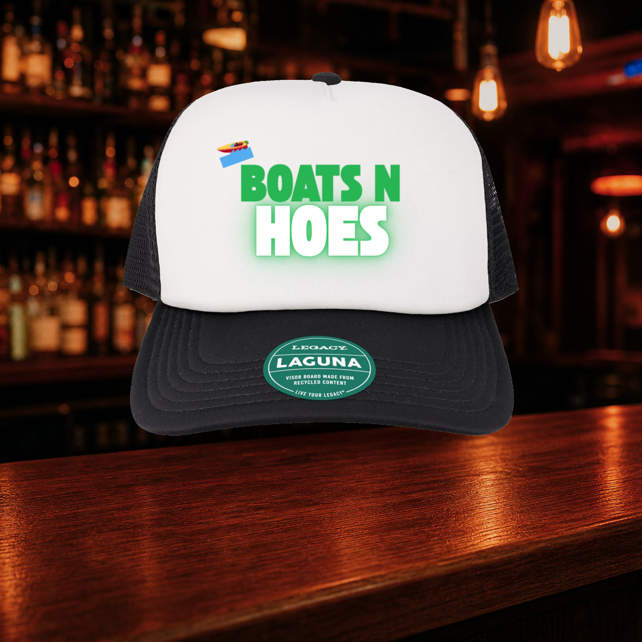 Boats N' Hoes Trucker Hat — Black variety shown against a warm after-dark bar backdrop