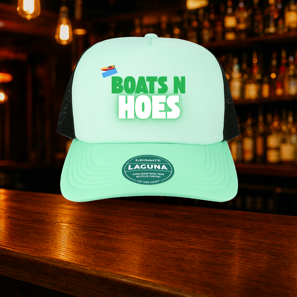 Boats N' Hoes Trucker Hat — Teal variety shown against a warm after-dark bar backdrop