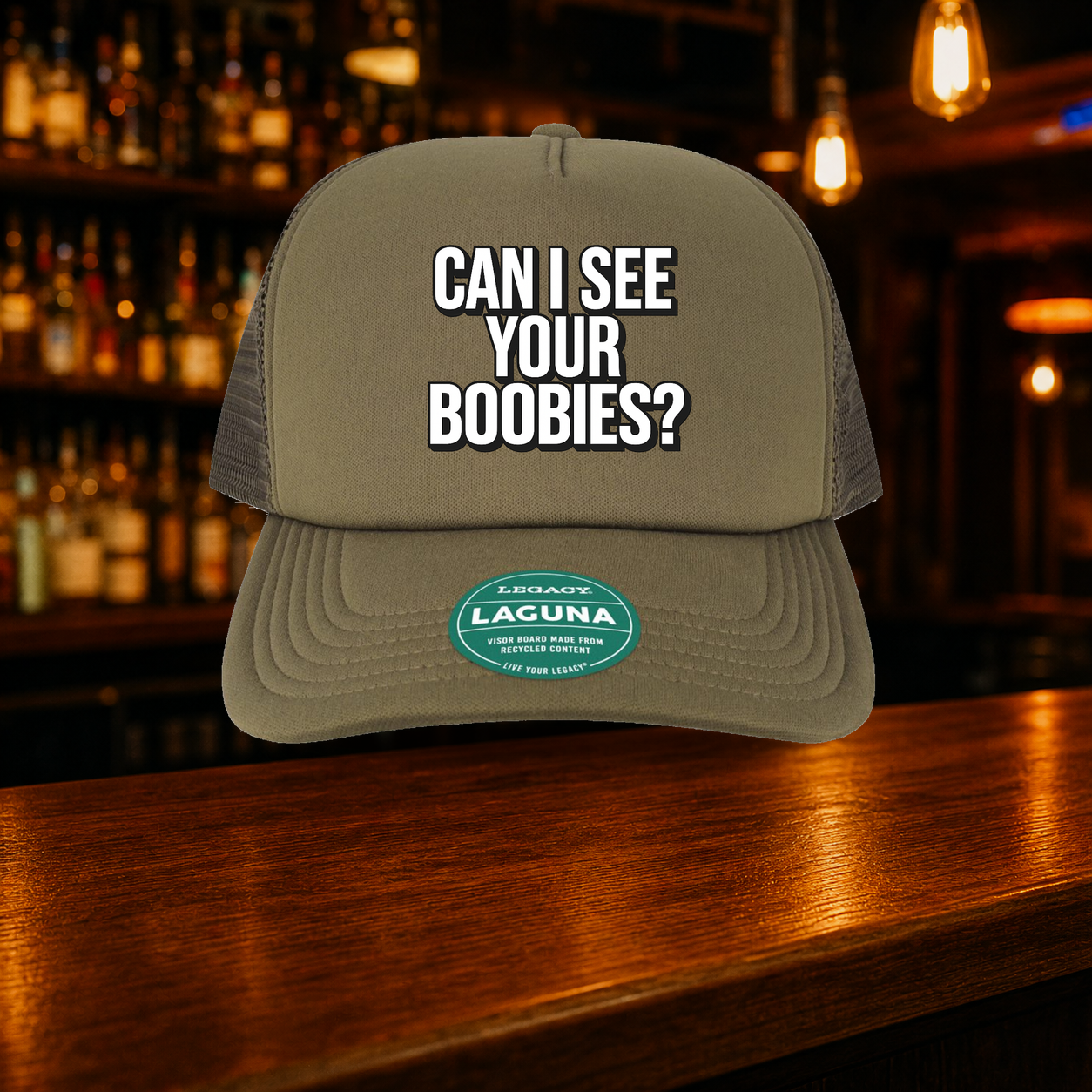 Can I See Your Boobs Trucker Hat shown against a warm after-dark bar backdrop