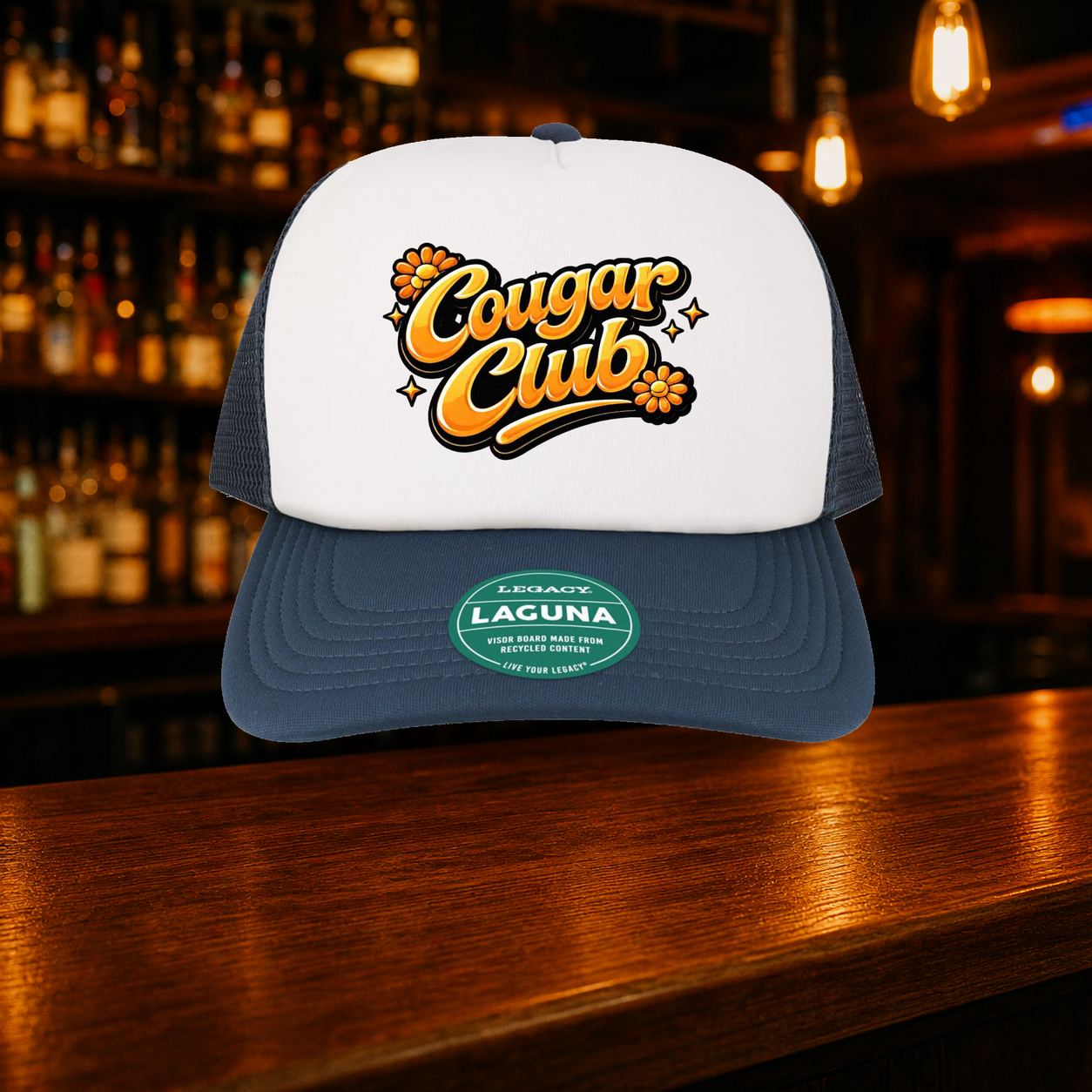 Cougar Club Trucker Hat — Navy variety shown against a warm after-dark bar backdrop