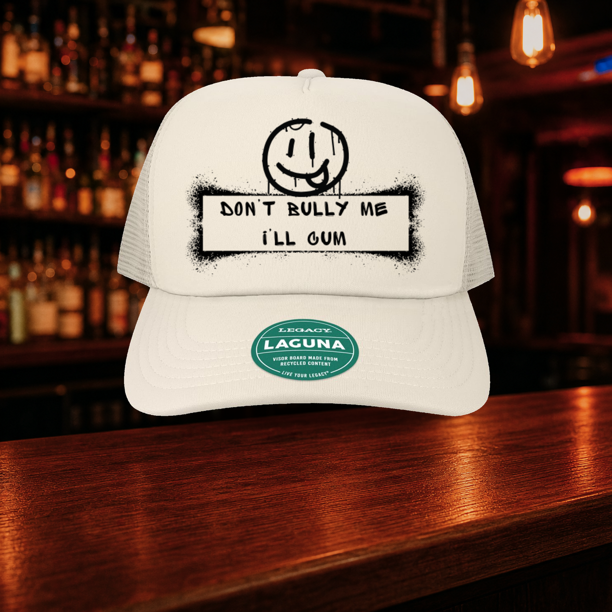 Don't Bully Me I'll Cum Trucker Hat — Beige variety shown against a warm after-dark bar backdrop