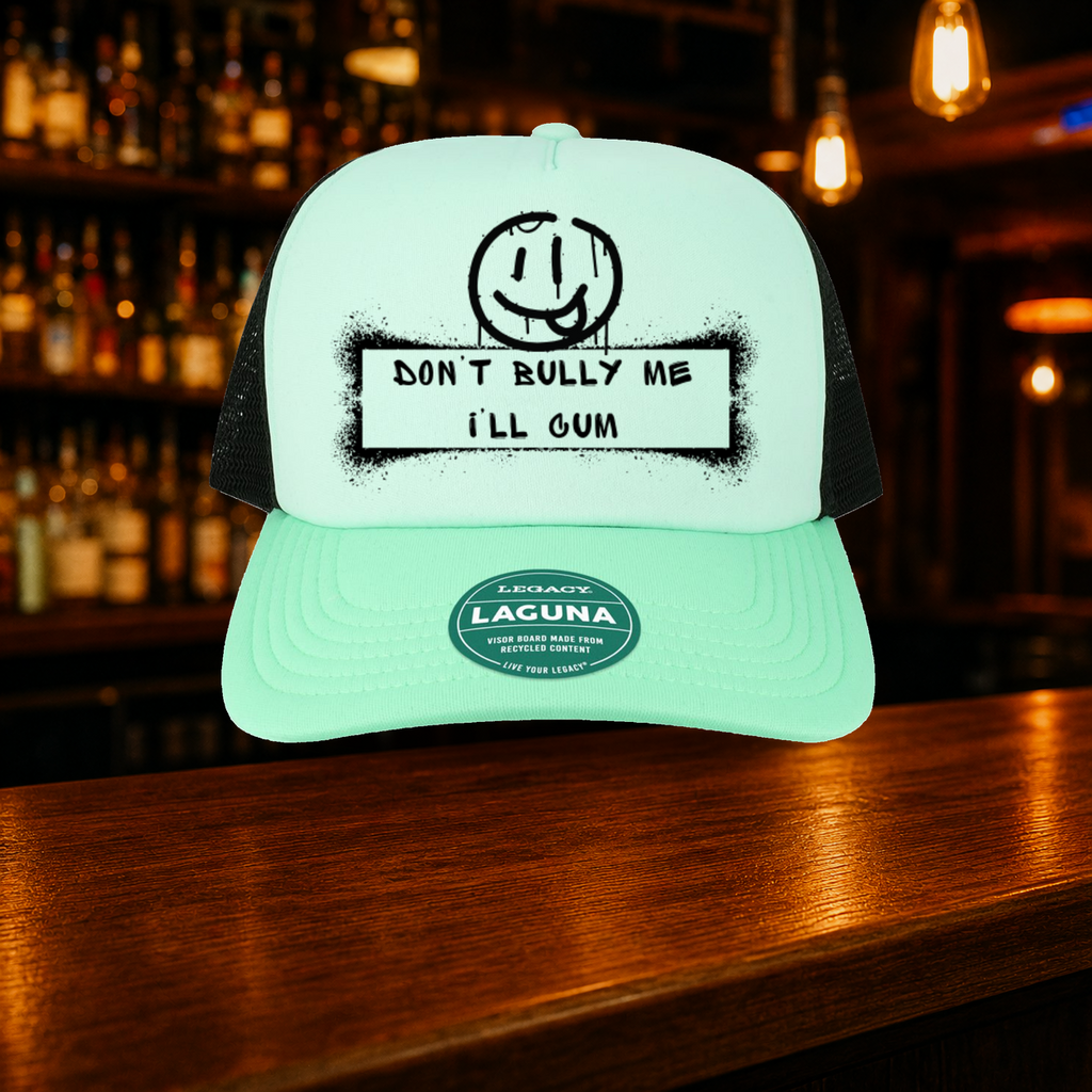 Don't Bully Me I'll Cum Trucker Hat — Teal variety shown against a warm after-dark bar backdrop