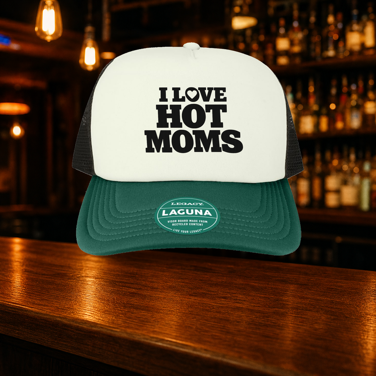 I Love Hot Moms Trucker Hat — Green variety shown against a warm after-dark bar backdrop