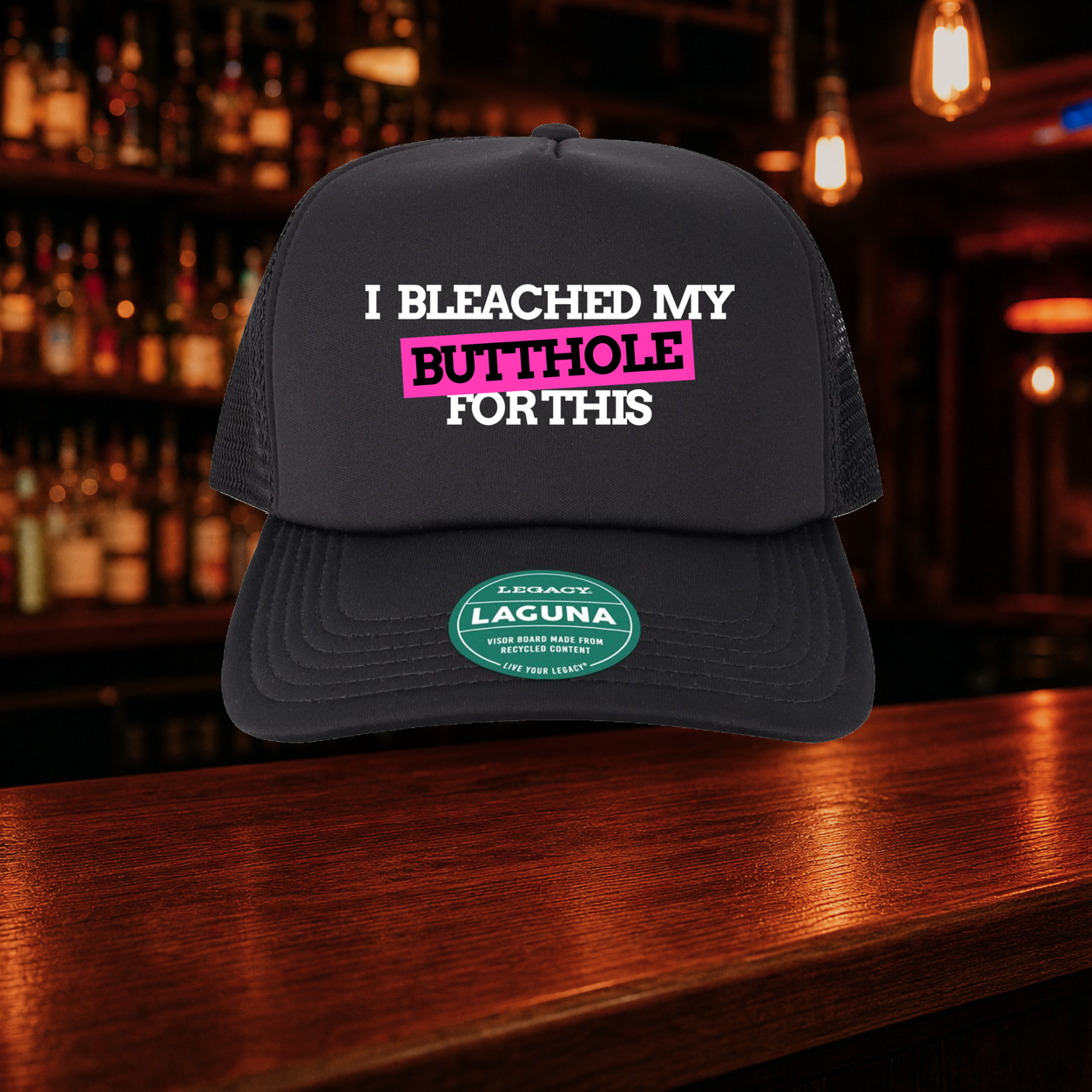 I Bleached My Butthole for This Trucker Hat shown against a warm after-dark bar backdrop