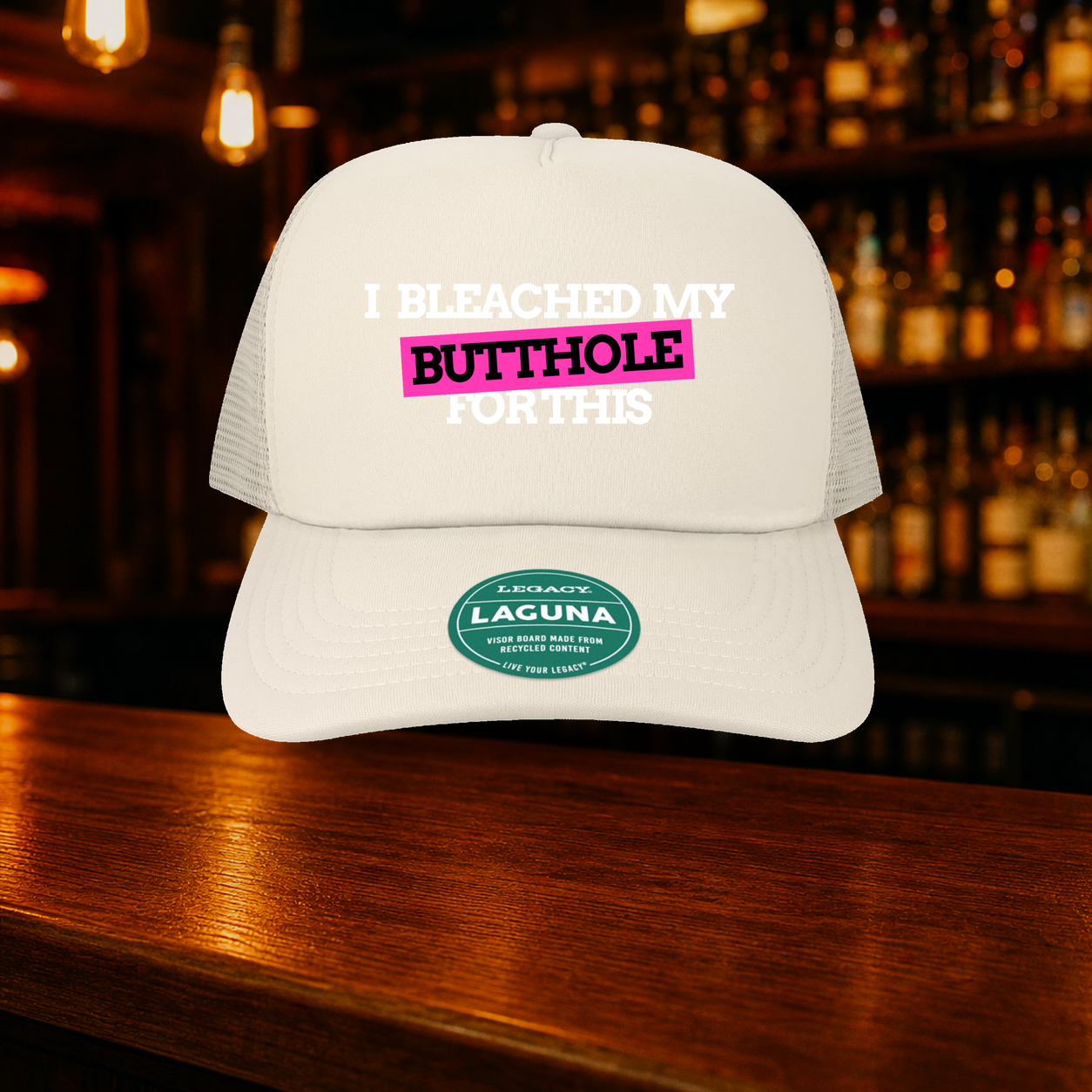I Bleached My Butthole for This Trucker Hat — Beige variety shown against a warm after-dark bar backdrop