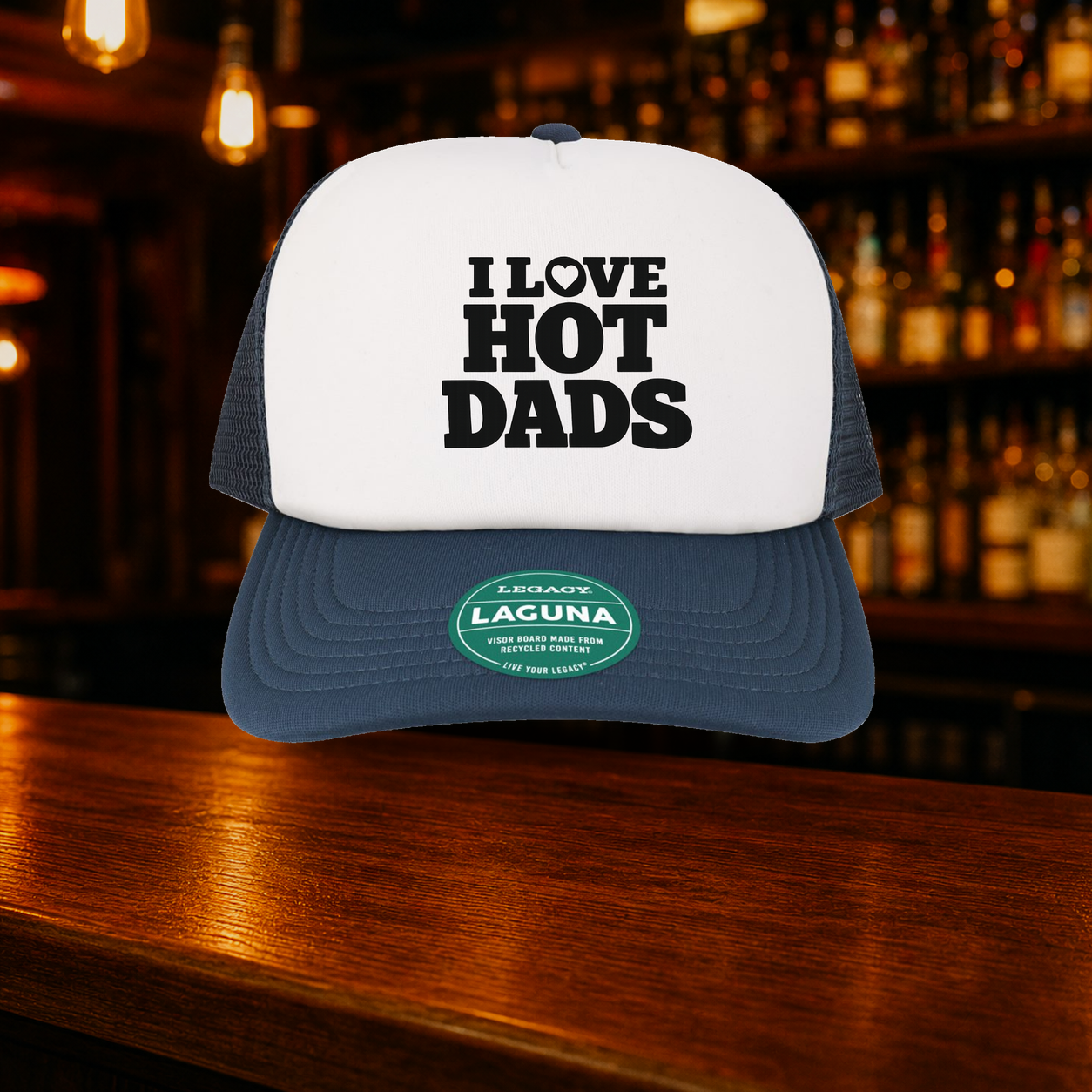 I Love Hot Dads Trucker Hat shown against a warm after-dark bar backdrop