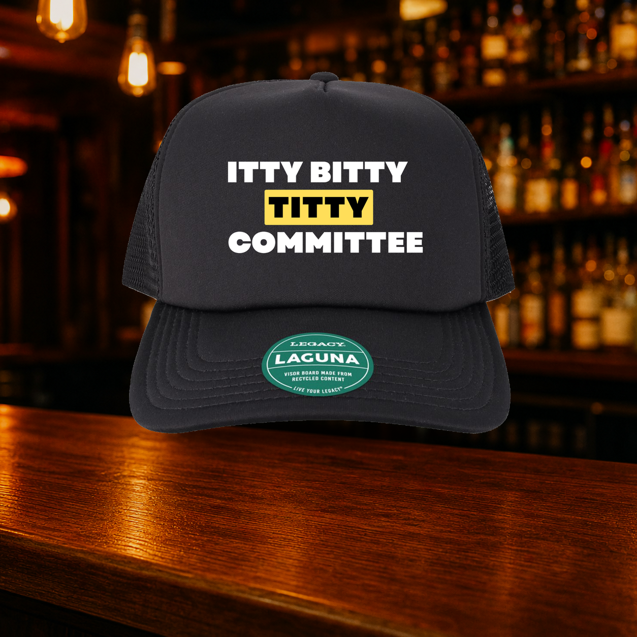 Itty Bitty Titty Committee Trucker Hat shown against a warm after-dark bar backdrop