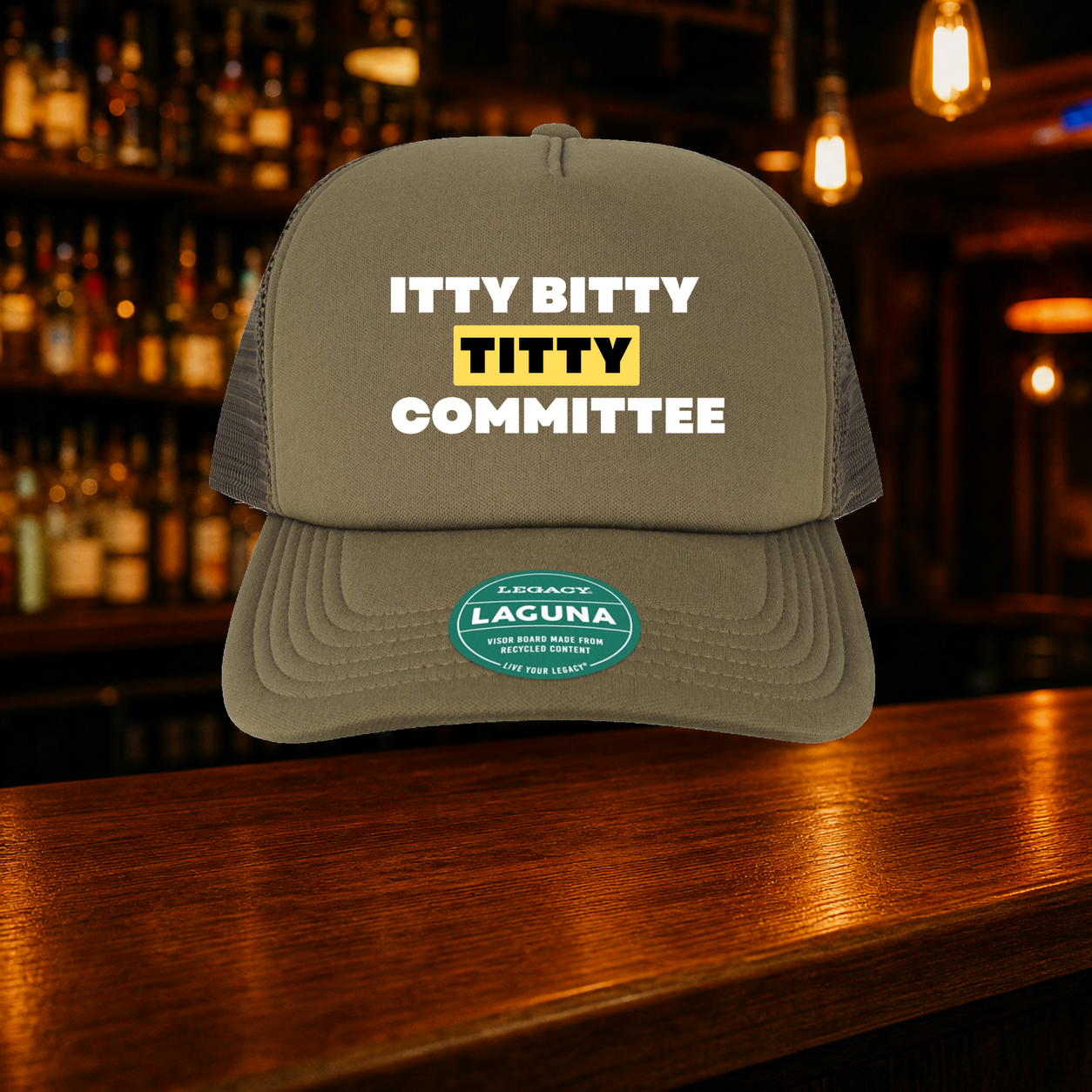 Itty Bitty Titty Committee Trucker Hat — Olive variety shown against a warm after-dark bar backdrop