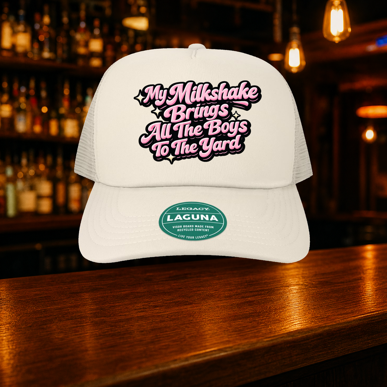My Milkshake Bring All the Boys to the Yard Trucker Hat shown against a warm after-dark bar backdrop