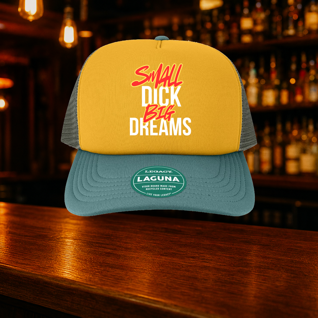 Small Dick Big Dreams Trucker Hat — Bronze variety shown against a warm after-dark bar backdrop