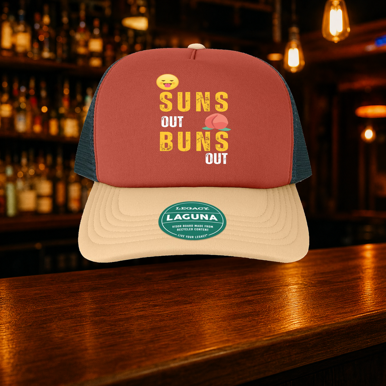 Suns Out Buns Out Trucker Hat shown against a warm after-dark bar backdrop