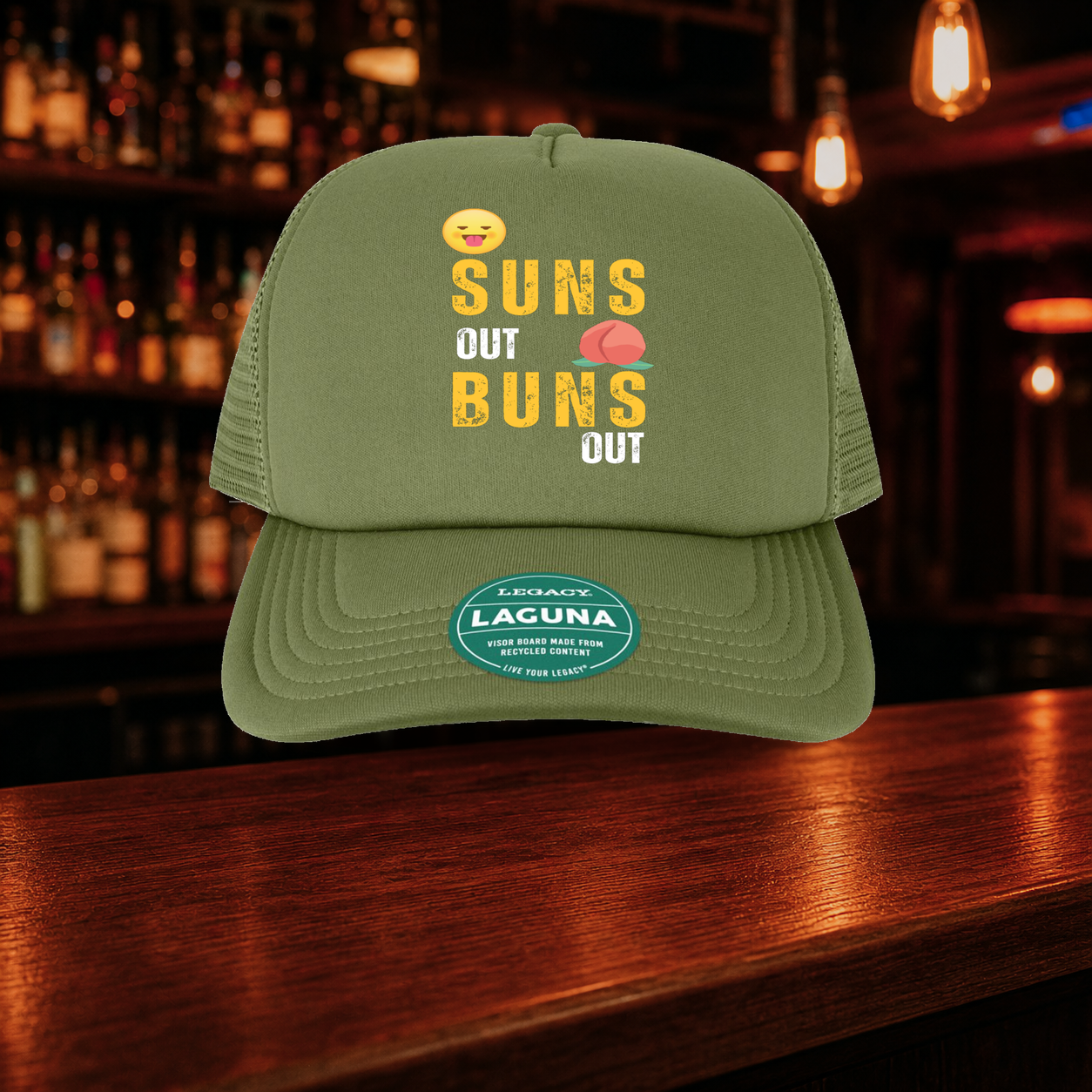 Suns Out Buns Out Trucker Hat — Olive variety shown against a warm after-dark bar backdrop