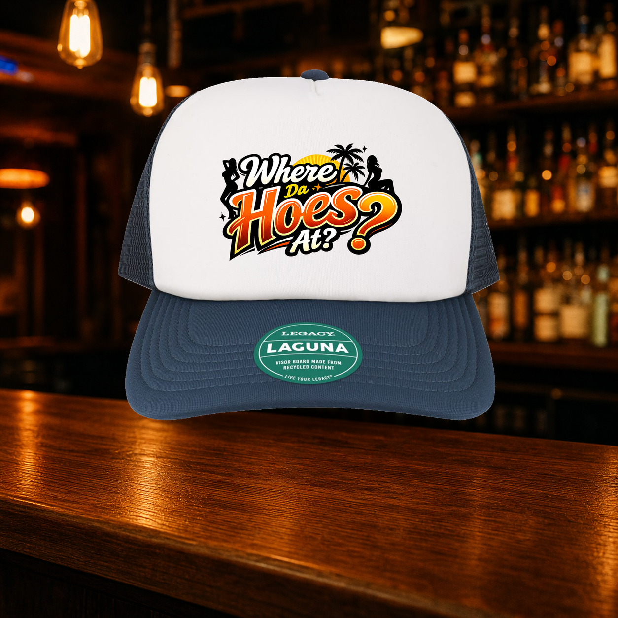 Where Da Hoes At? Trucker Hat shown against a warm after-dark bar backdrop
