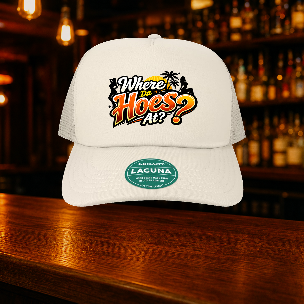 Where Da Hoes At? Trucker Hat — Beige variety shown against a warm after-dark bar backdrop