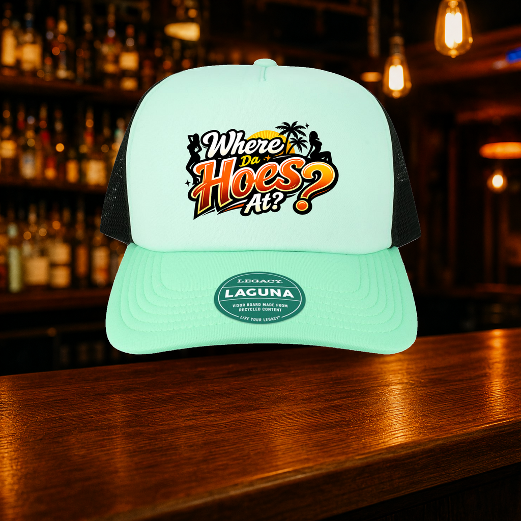 Where Da Hoes At? Trucker Hat — Teal variety shown against a warm after-dark bar backdrop